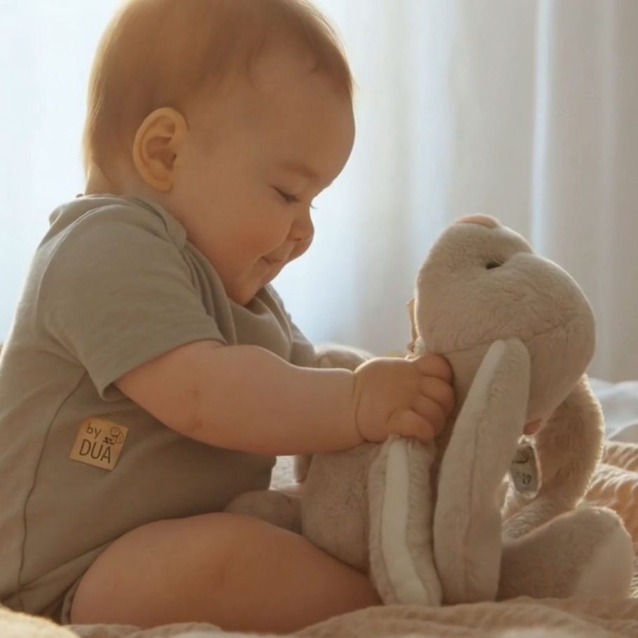 Lächelndes Baby, das mit einem plüschigen Hasen spielt. by DUA Babyartikel Lächelndes Baby, das mit einem plüschigen Hasen spielt. by DUA Babyartikel